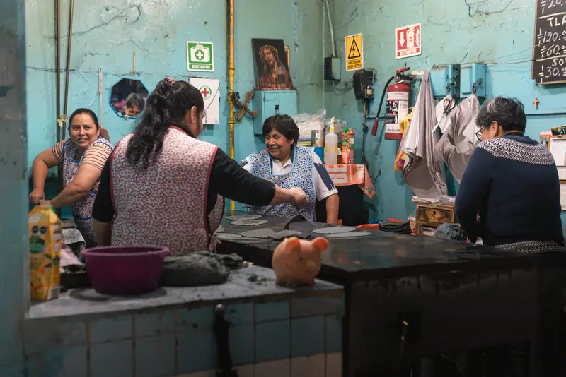 Three women laughing together in a turquoise-walled kitchen during prep